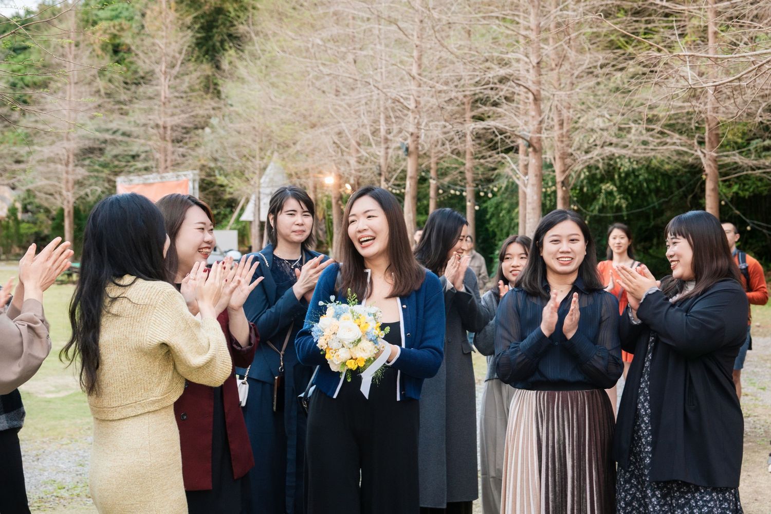 A group of wedding guests stands together in a line outdoors during a celebration.