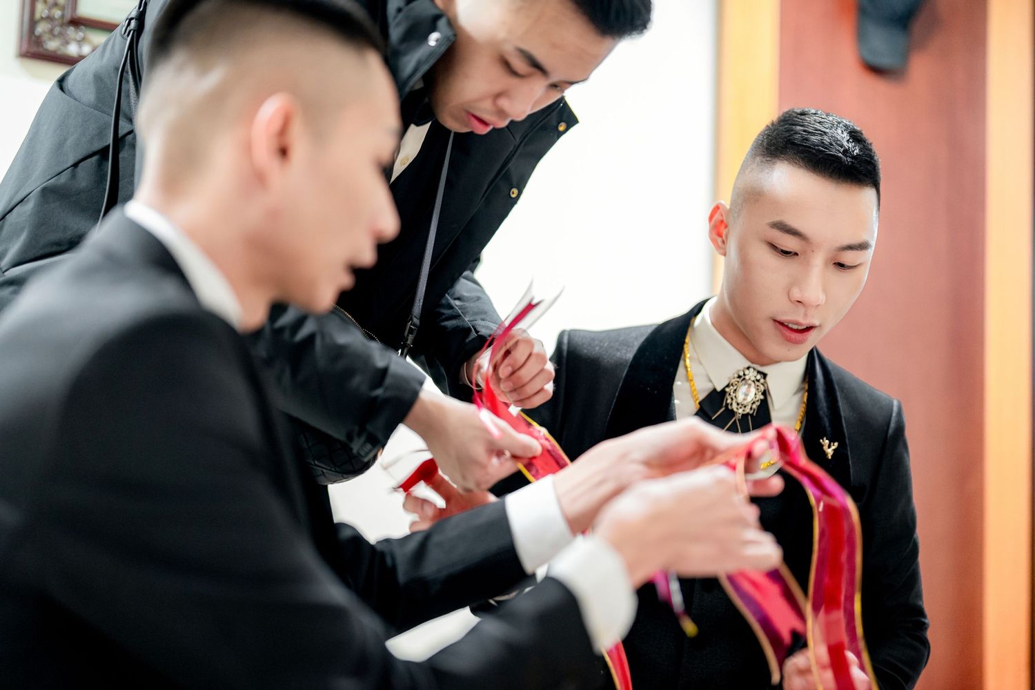 A professional barber in a black shirt carefully styles a client's hair with precision tools in a well-lit salon.