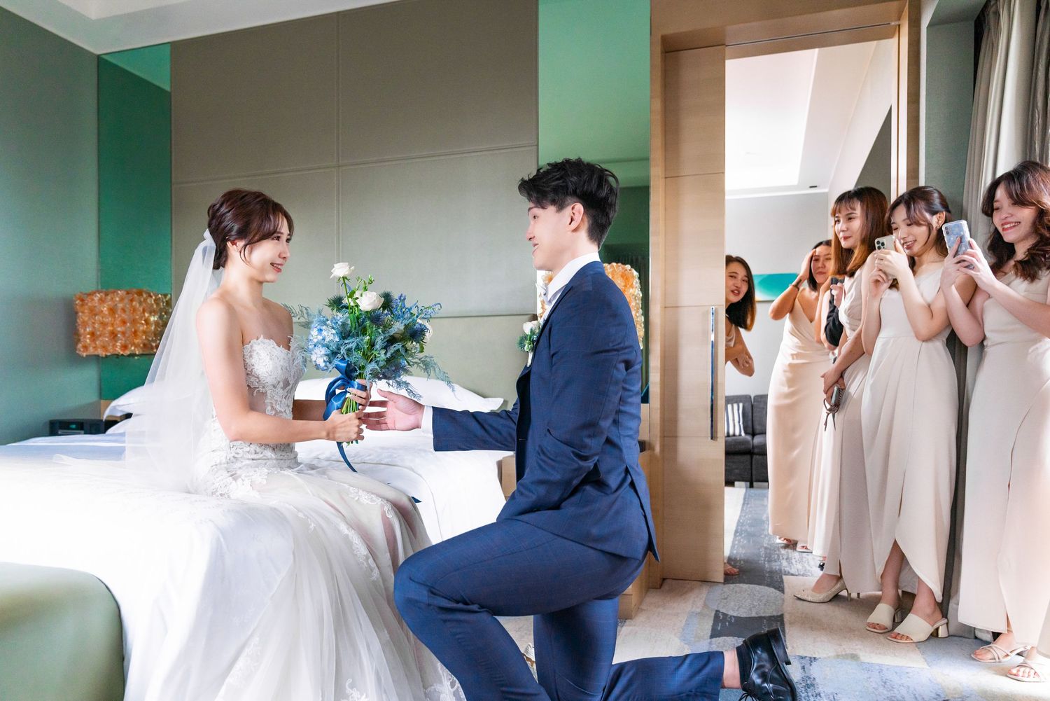 A wedding scene in a mint green room with a couple exchanging rings while bridesmaids in white dresses watch from doorway.