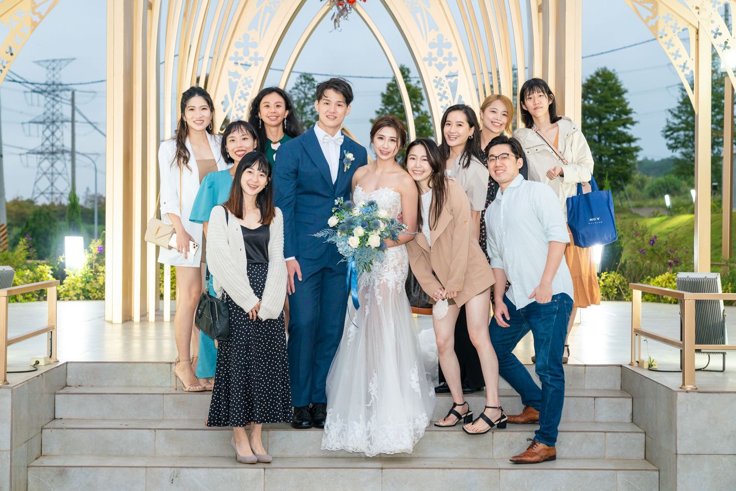 Wedding party poses together on white gazebo steps during outdoor summer celebration.