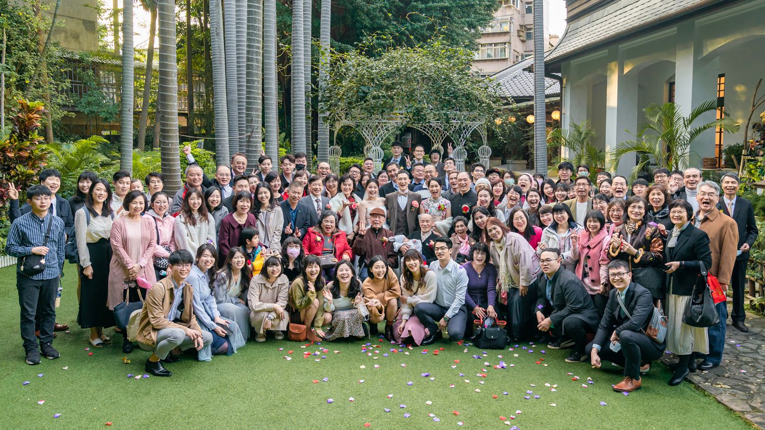 Large group photo of people gathered outdoors on green lawn in front of building during daytime event.