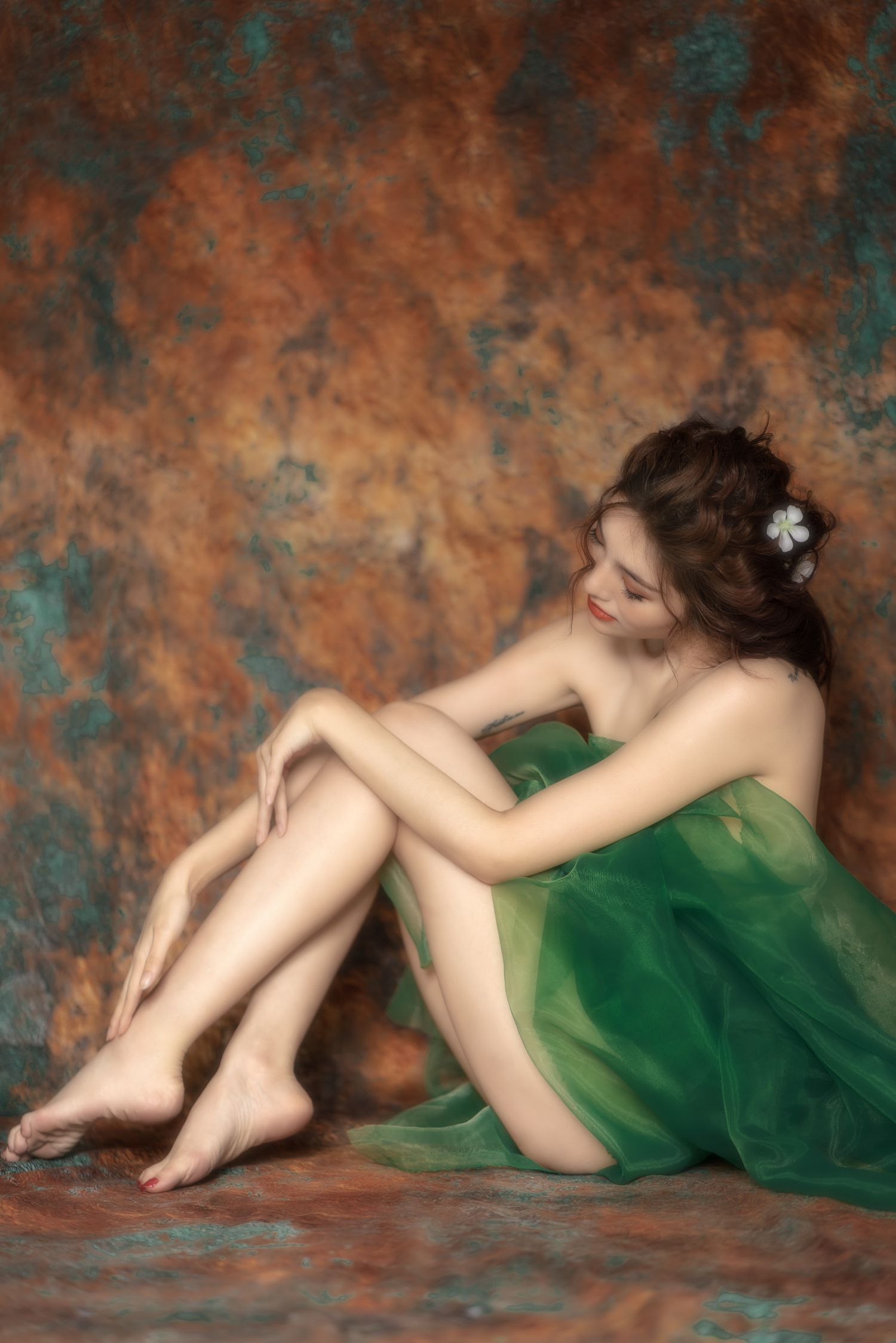 Fine art portrait of figure in flowing emerald green dress reclining against textured copper and teal backdrop.