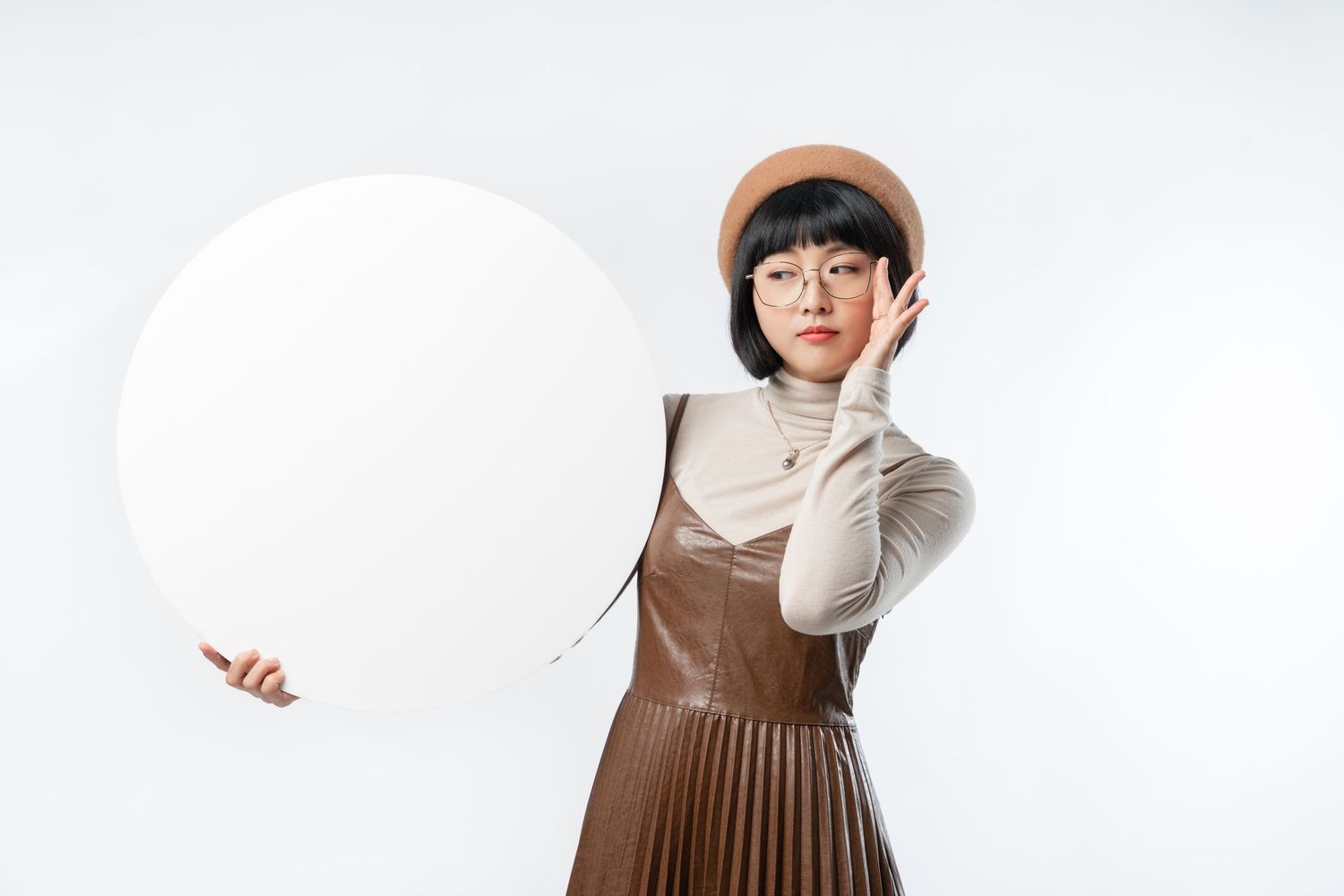 Person in brown dress and turtleneck holding large white balloon against white background.