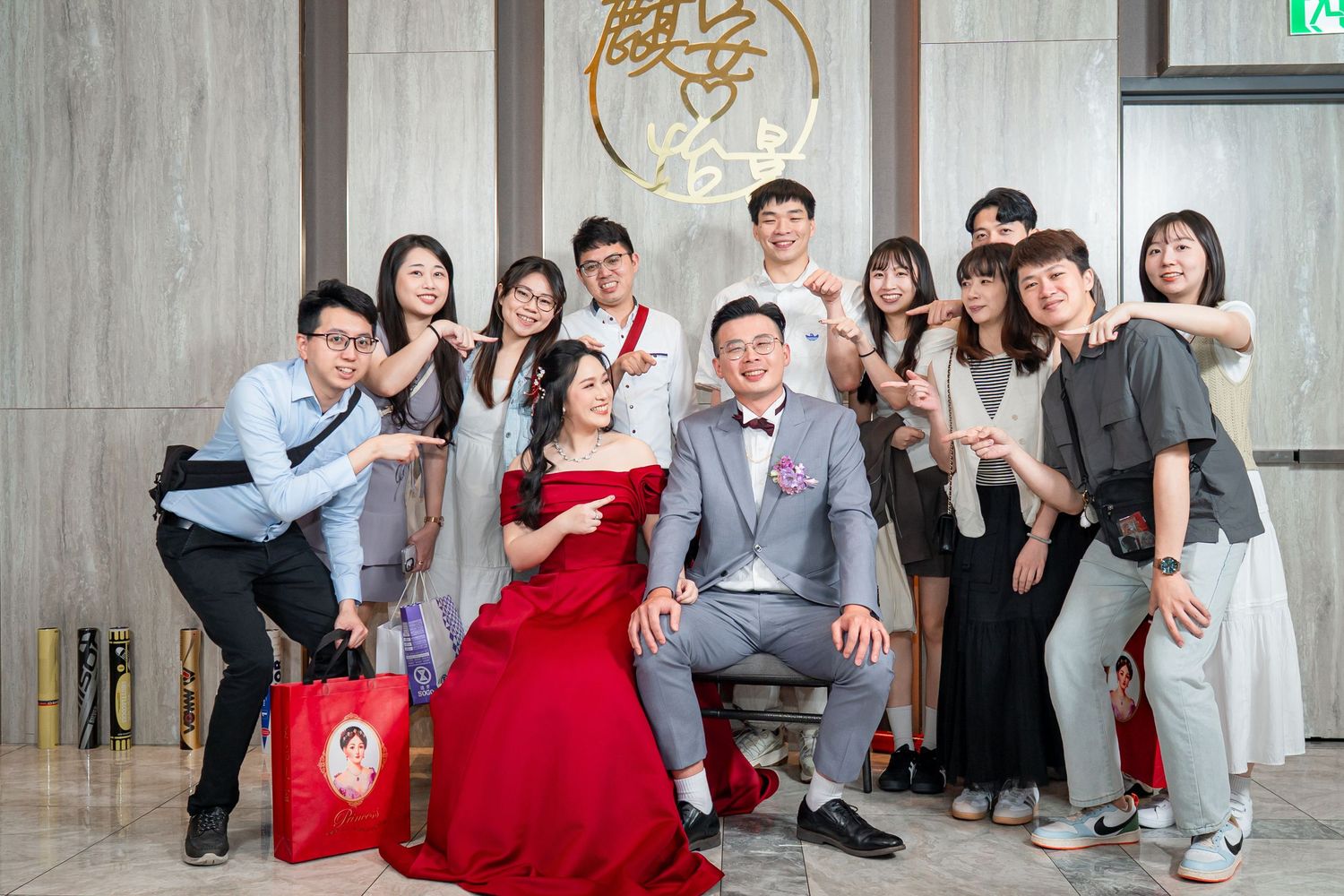 Group of people posing together at a formal event with one person wearing a red gown and another in a gray suit.