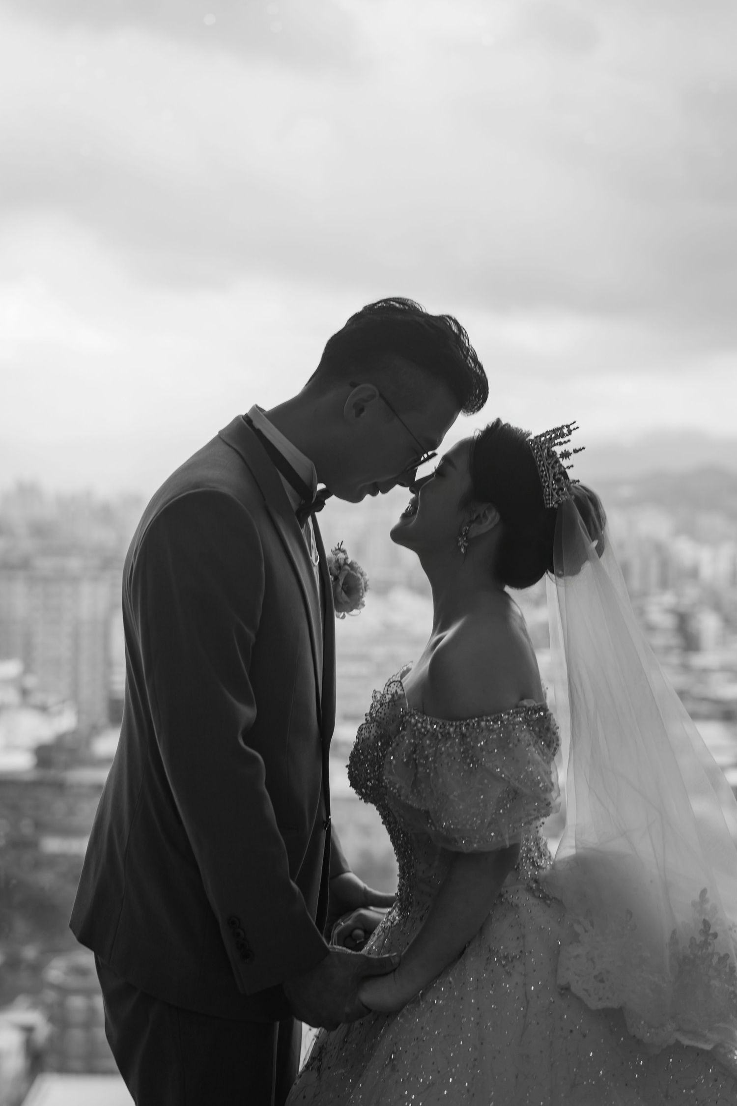 A black and white wedding portrait showing a tender moment between a bride in a sparkly gown and groom against a cityscape.