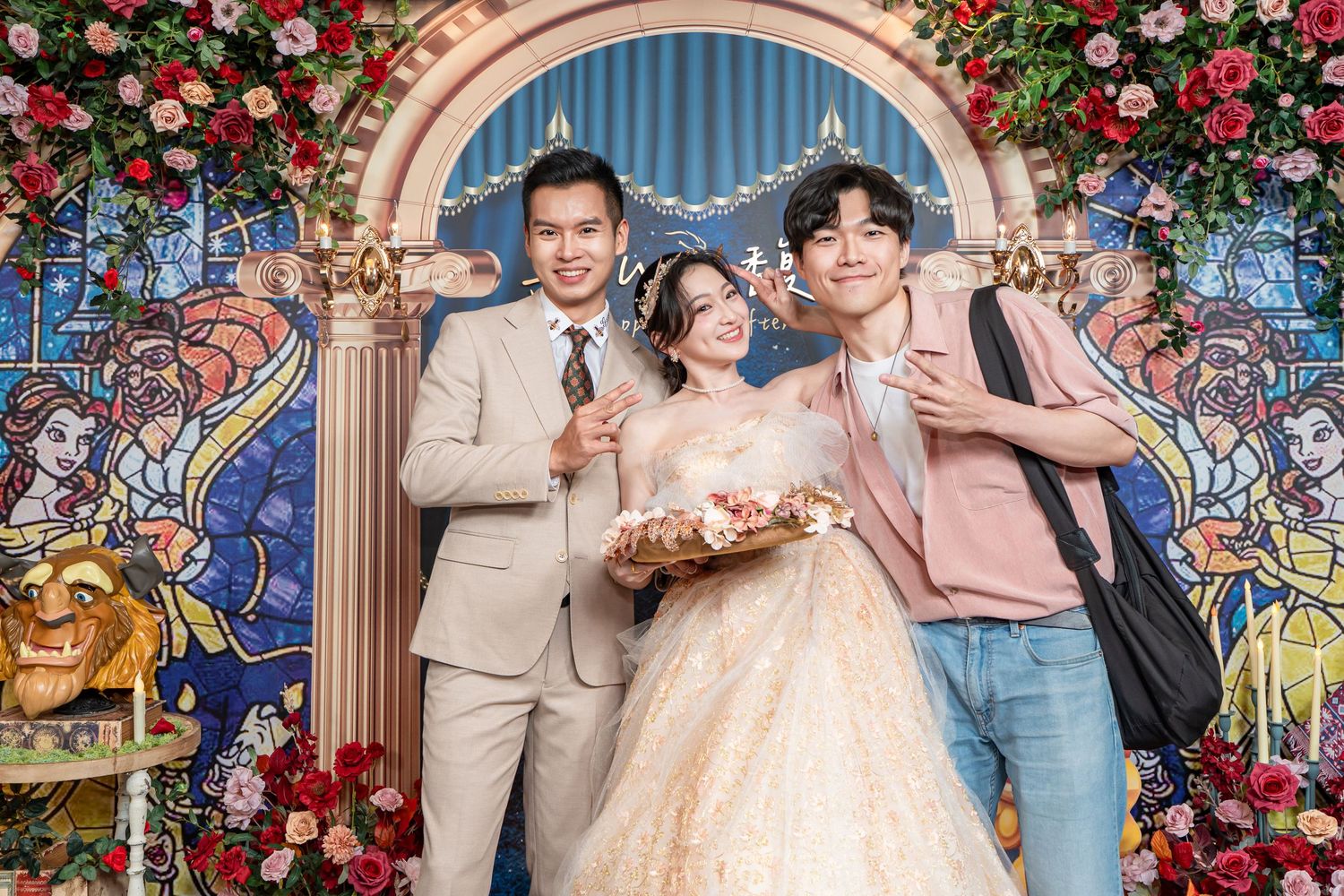 Bride in golden gown poses with two men at Beauty and the Beast themed wedding with stained glass backdrop.