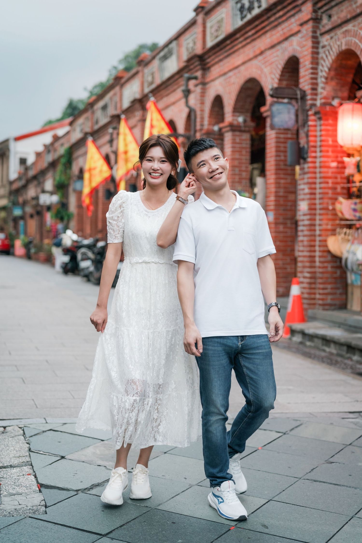A couple walks along a historic red brick arcade street with Chinese lanterns and flags in Taiwan.