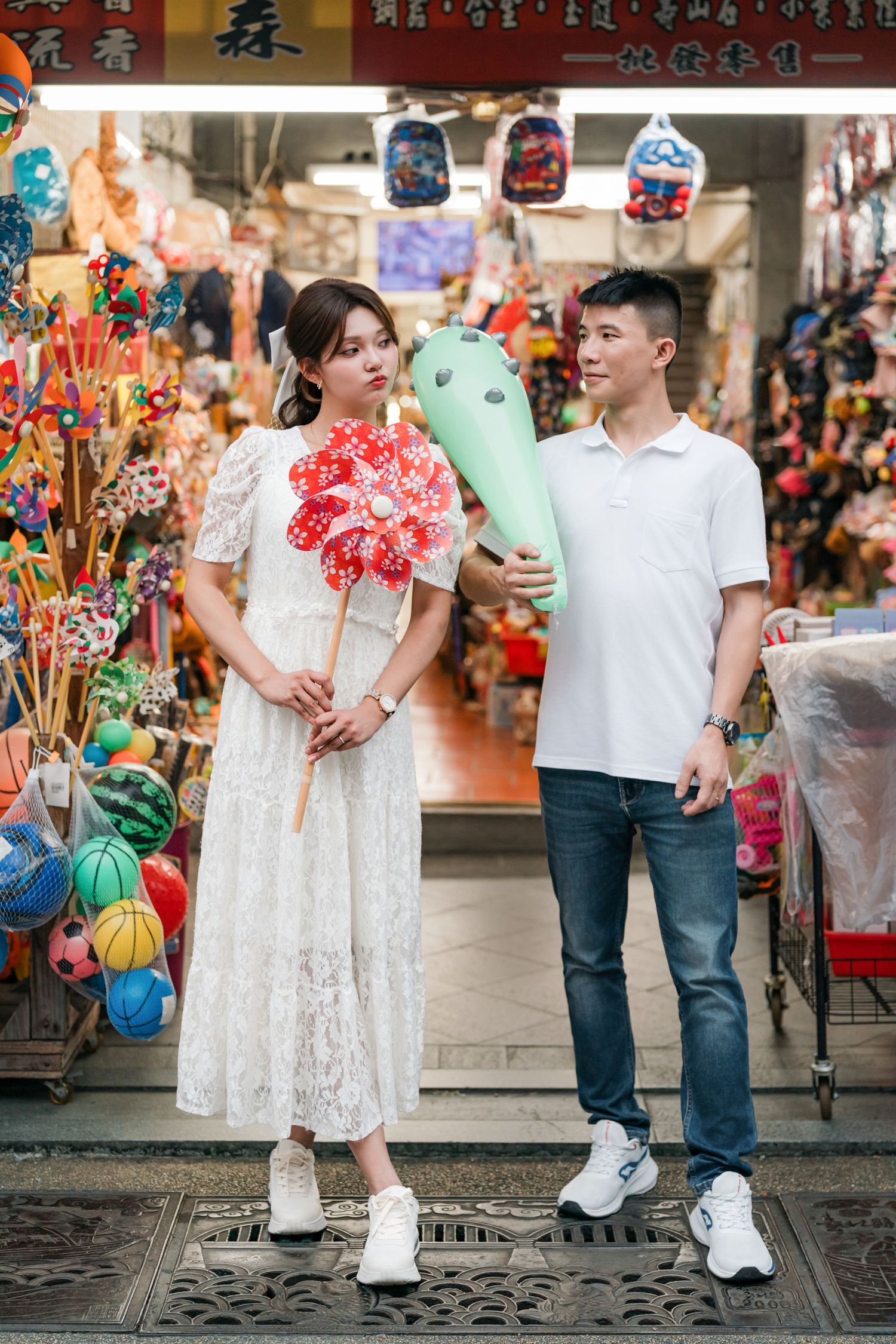 Couple in white outfits poses together at an Asian marketplace with traditional decorations and lanterns.