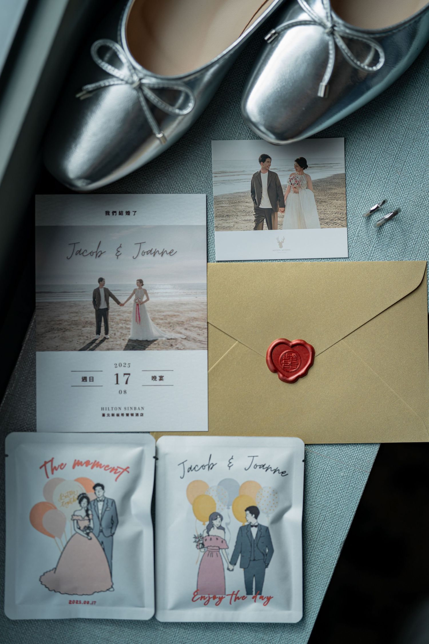 Wedding details flatlay with silver ballet flats, invitation cards, love letter with red wax seal, and beach photo.