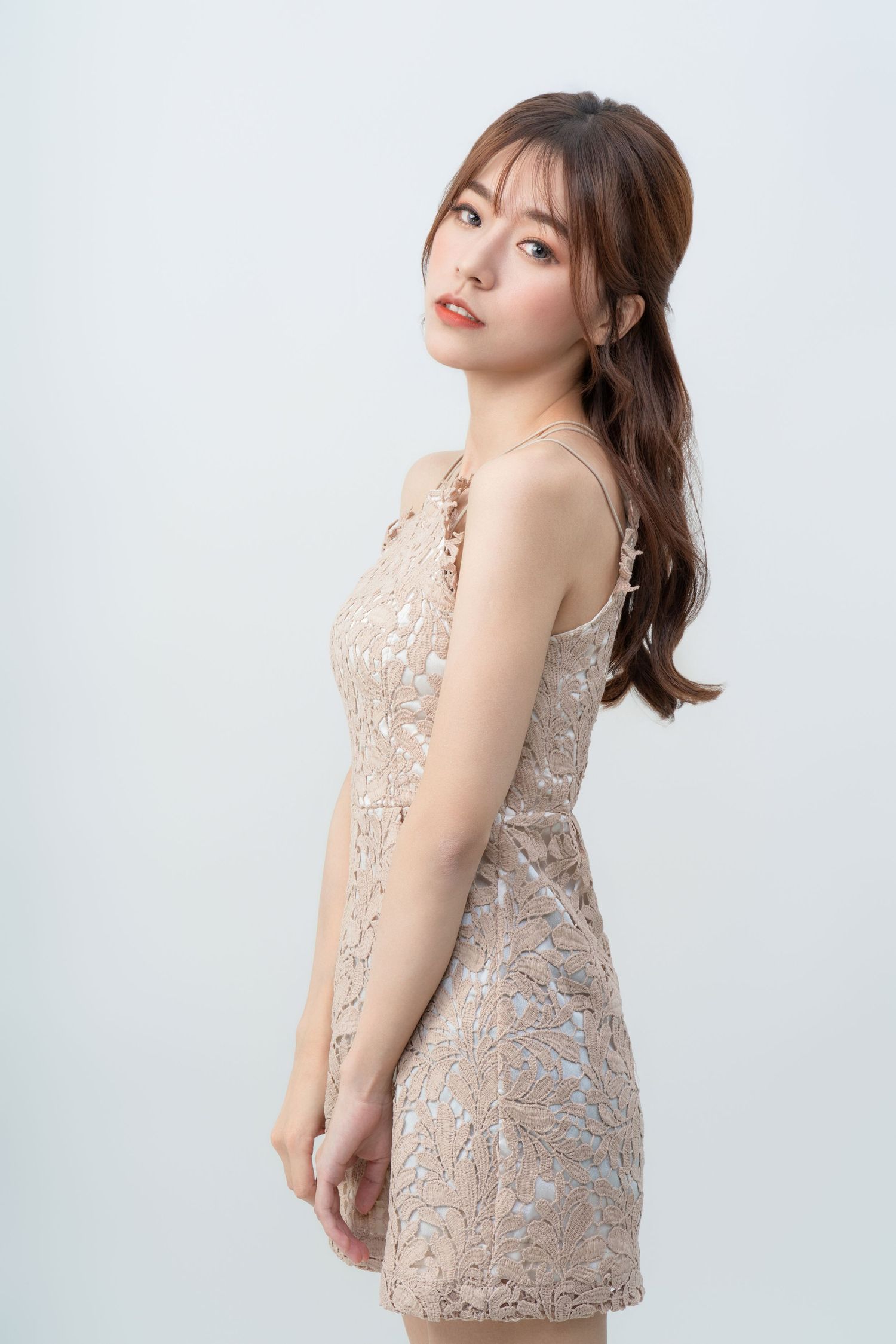 A young woman poses in an elegant beige lace dress against a white studio background.