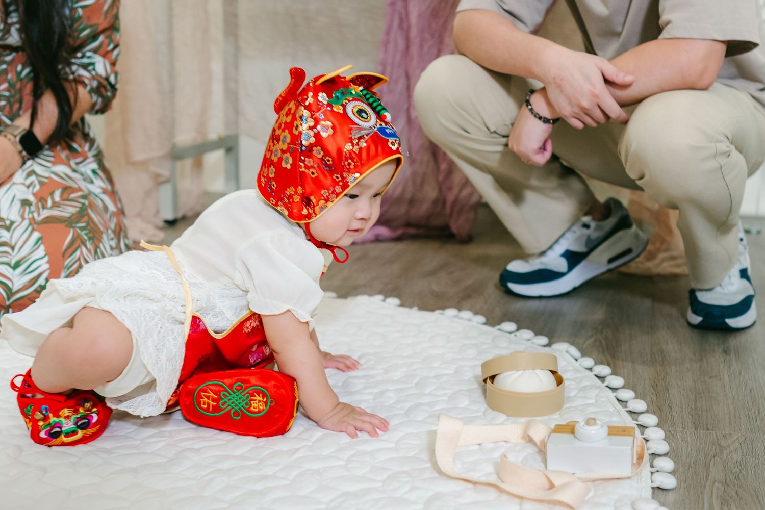 Little one in bright red traditional Chinese outfit sits on floor with wooden blocks and learning materials.