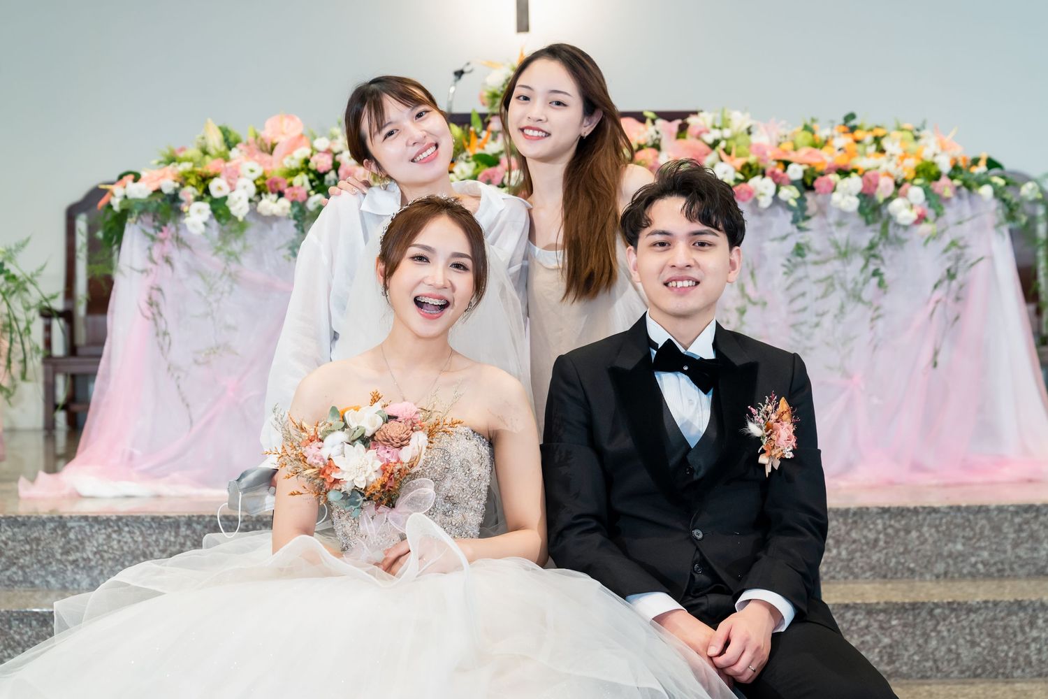 Wedding portrait in front of pink floral arch with decorative backdrop in church setting.