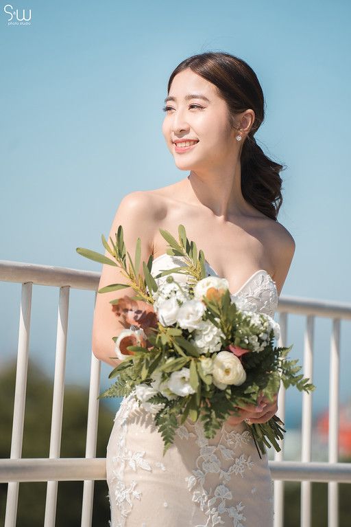Beautiful bridal portrait featuring a strapless lace dress and natural bouquet against blue sky.