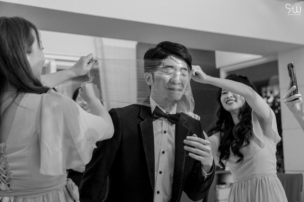 Wedding preparations showing joyful moments in black and white as attendees help with final touches before ceremony.