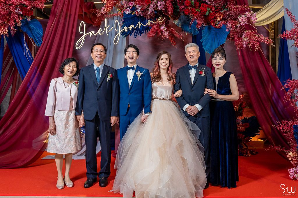Family formal portrait against wedding backdrop with red florals and blue drapery.