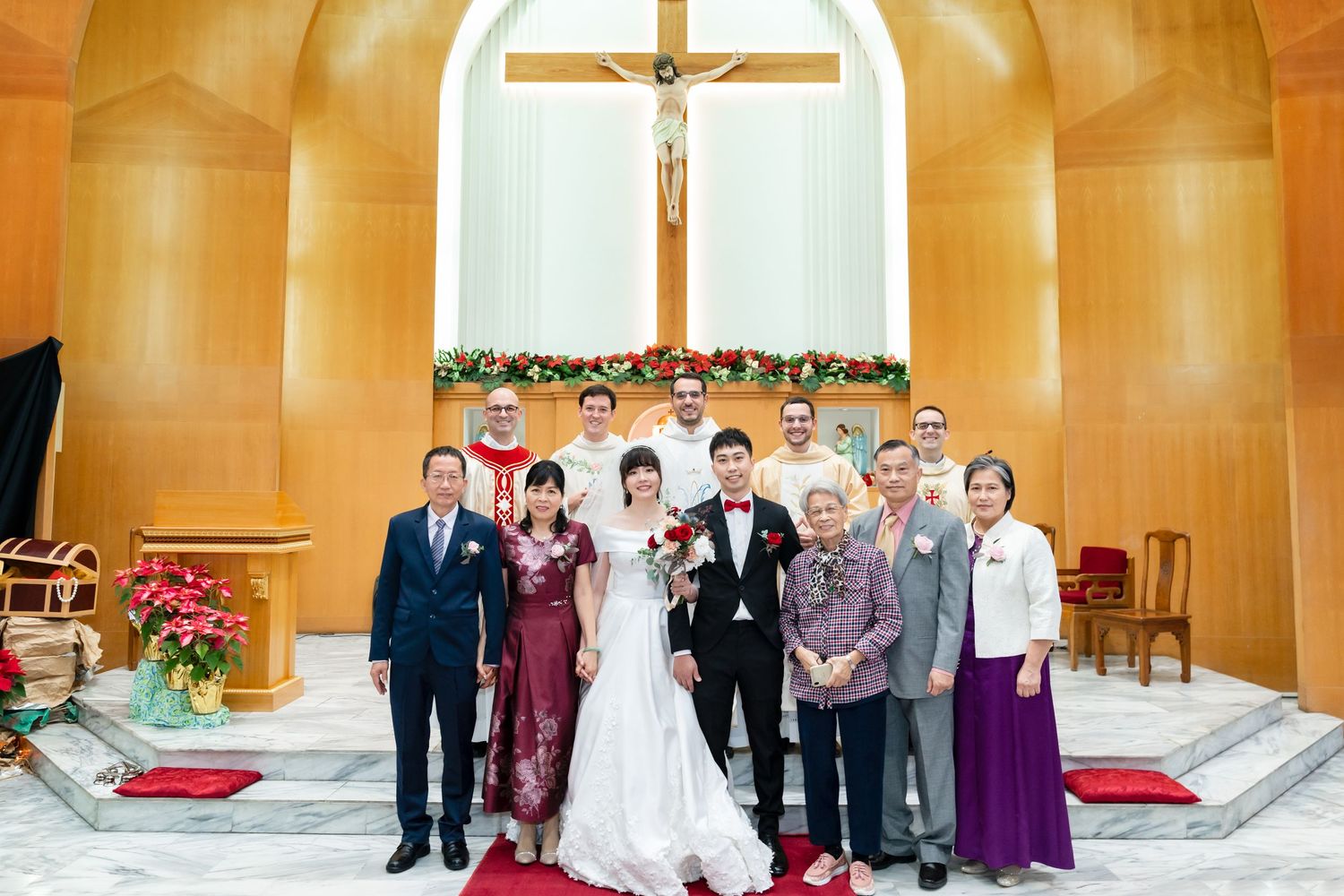 Wedding party gathered at church altar with golden walls and crucifix in background.