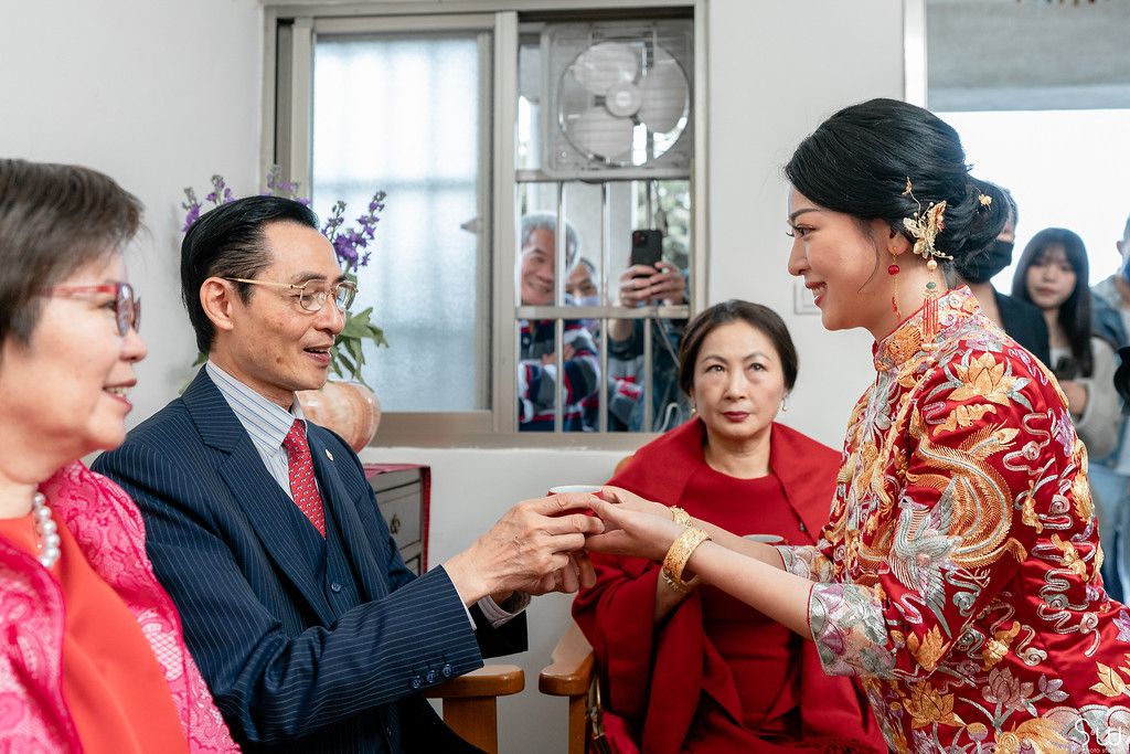 Tea ceremony participants exchange cups while others watch during traditional Chinese celebration.