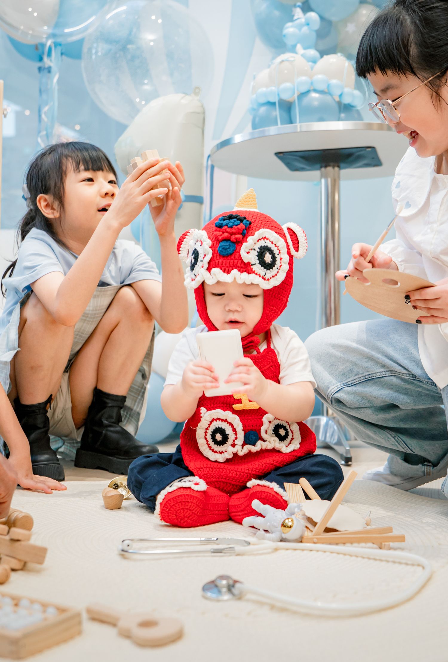 Children playing with wooden toys and a red plush toy on the floor in a bright modern space.