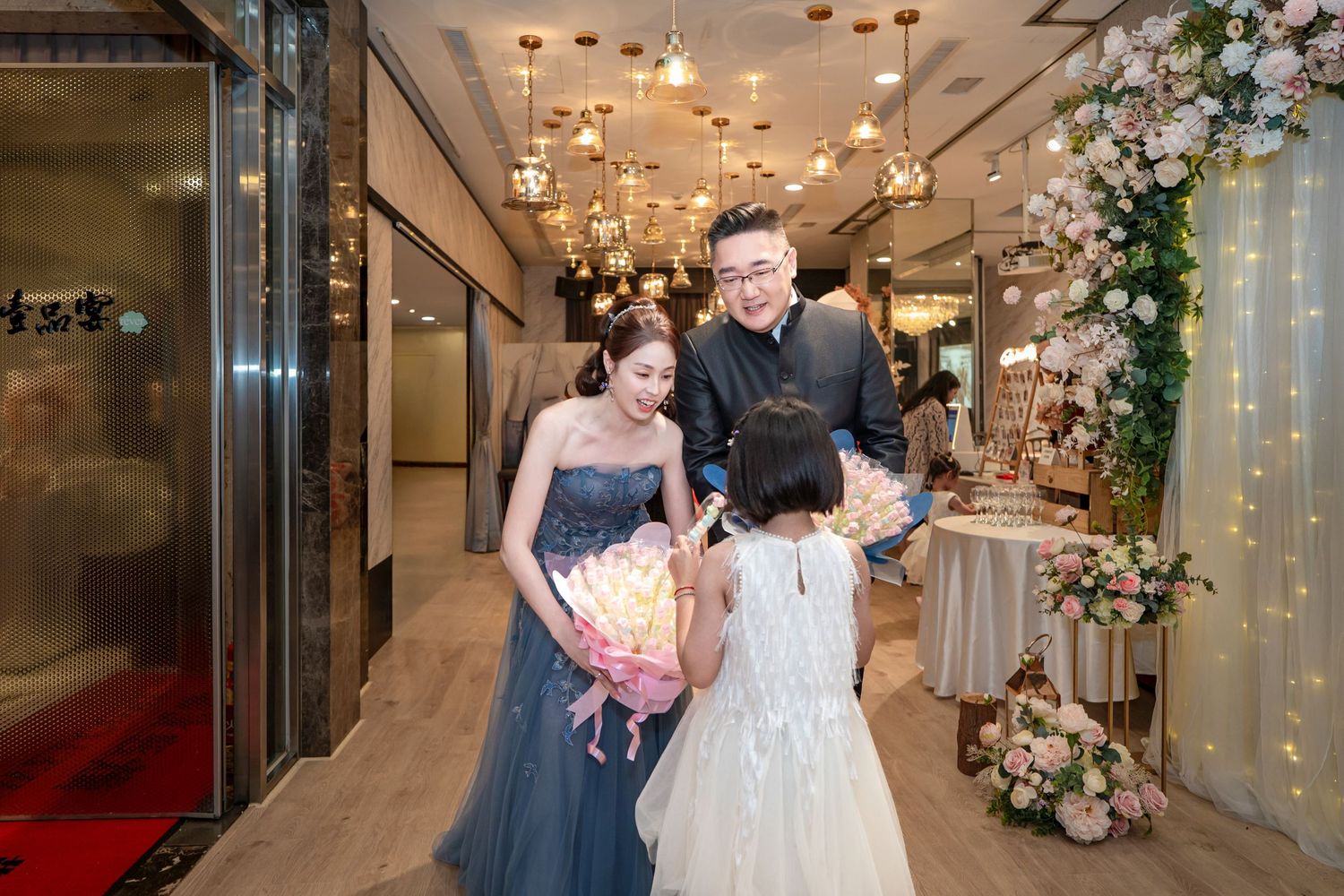 Wedding couple walks down elegant hotel hallway decorated with floral arrangements and crystal chandeliers.