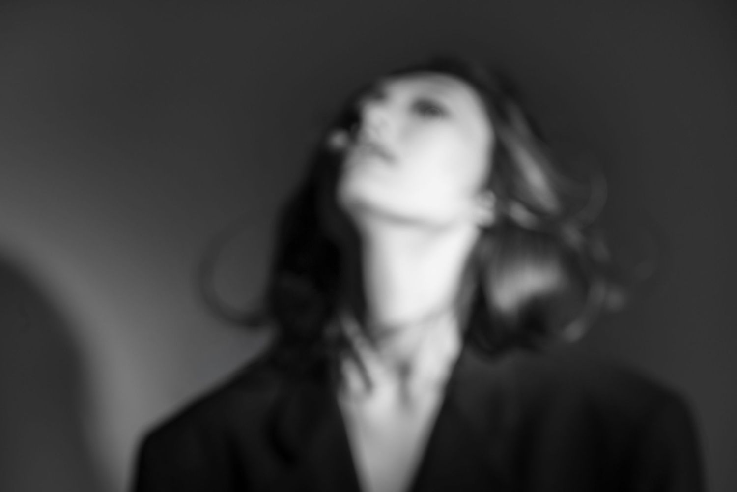 Black and white blurred portrait of a woman with head tilted back, dark hair flowing, wearing a black jacket.