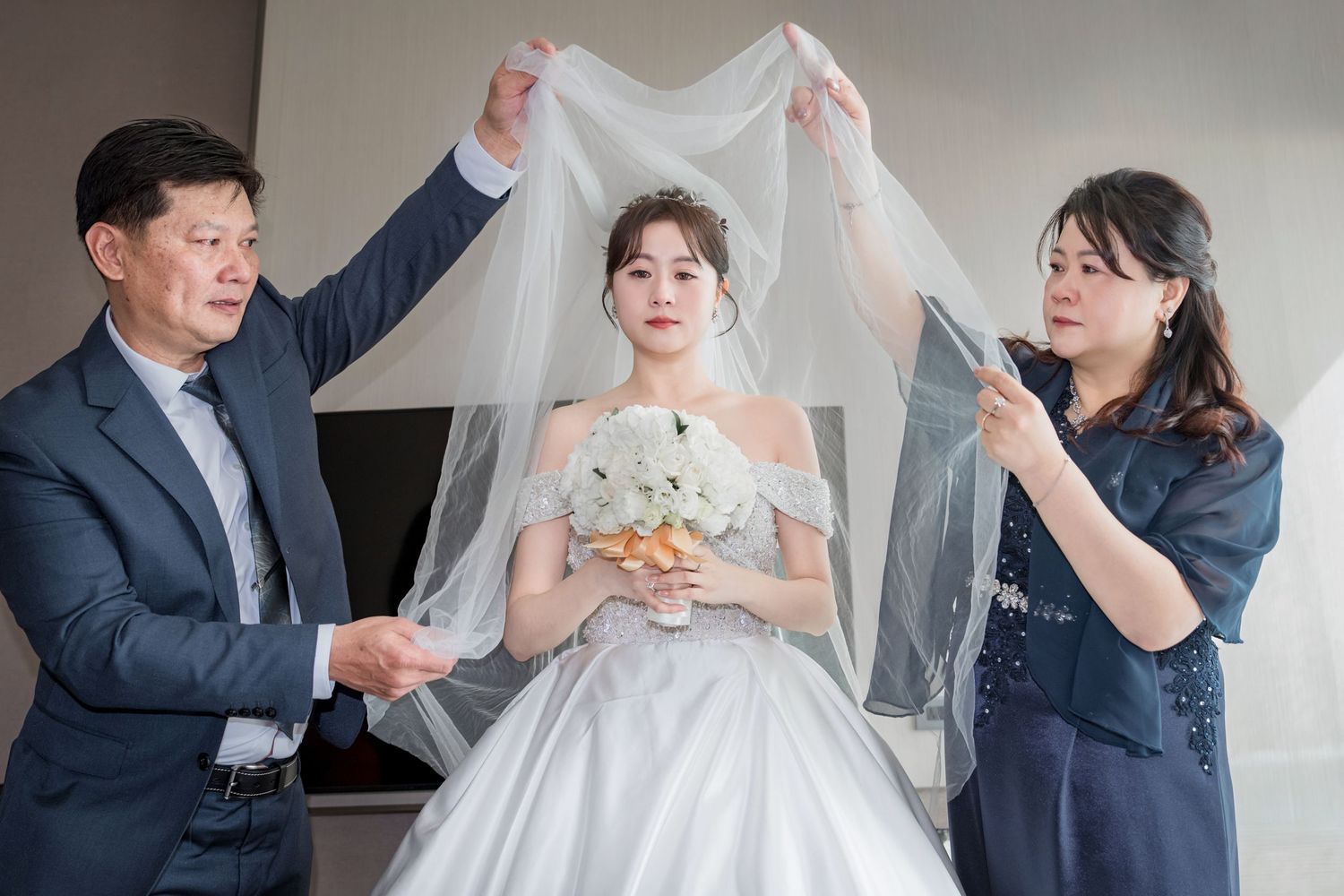 A wedding scene shows people helping with a white bridal veil and dress during preparation moments.