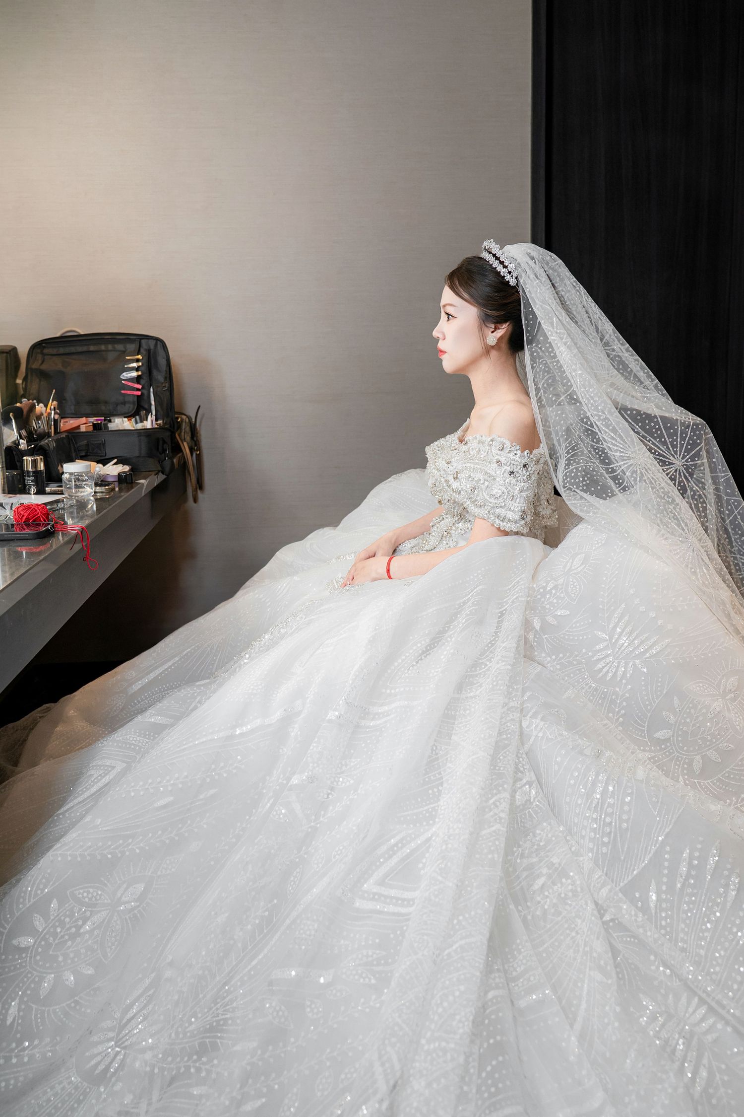 A stunning white wedding gown with intricate lace details and a flowing cathedral veil photographed in a dramatic side profile.
