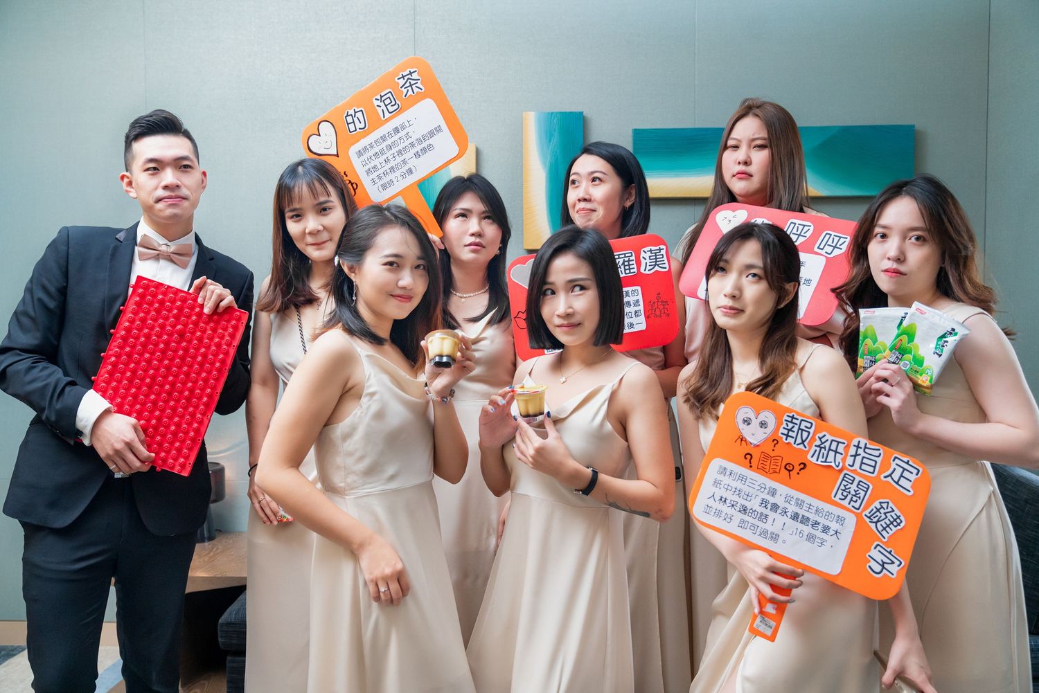 A group in formal attire poses together while holding colorful photo frames and signs at an indoor event.