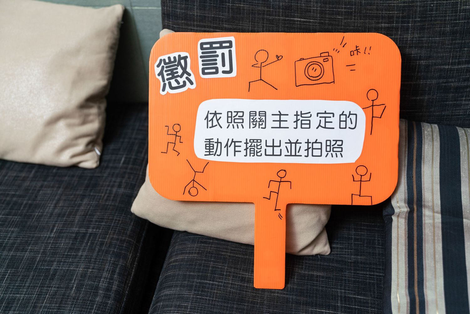 An orange speech bubble shaped sign with Chinese text sits on a gray couch cushion.