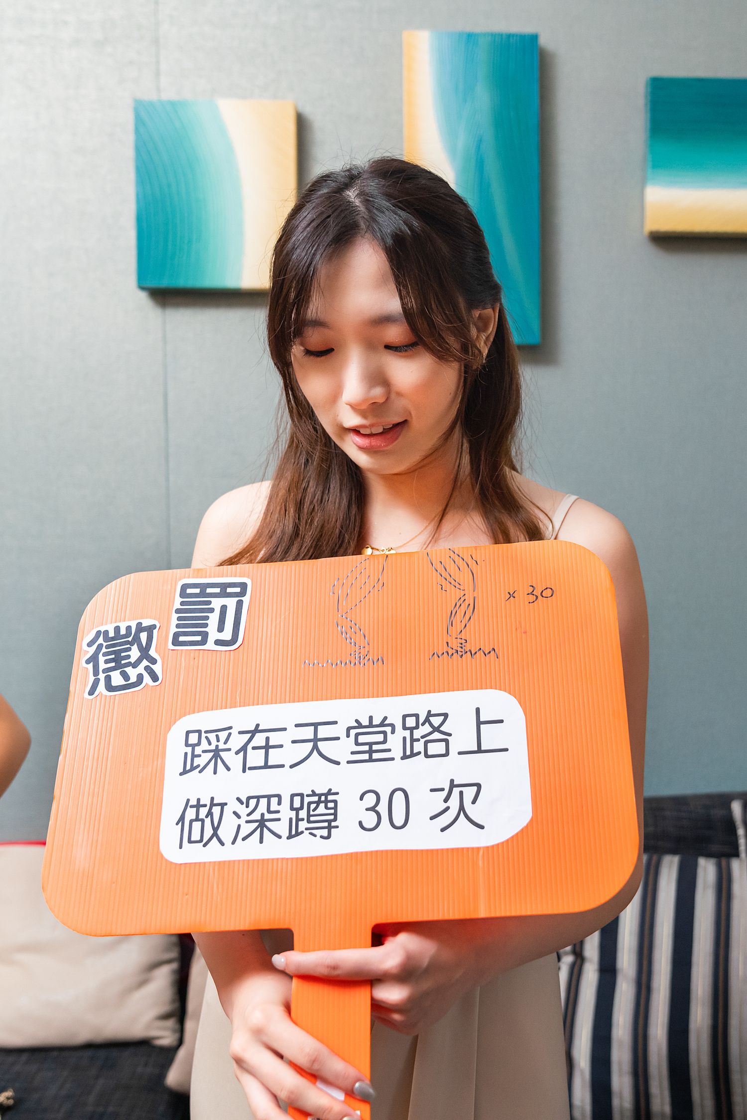 Someone holds up an orange sign with Chinese text on it against a wall decorated with teal and white artwork.