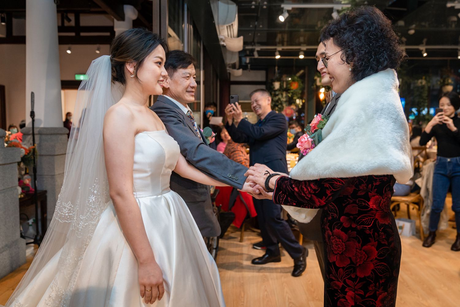 A wedding celebration scene with the bride in white dress interacting with guests at an indoor venue.