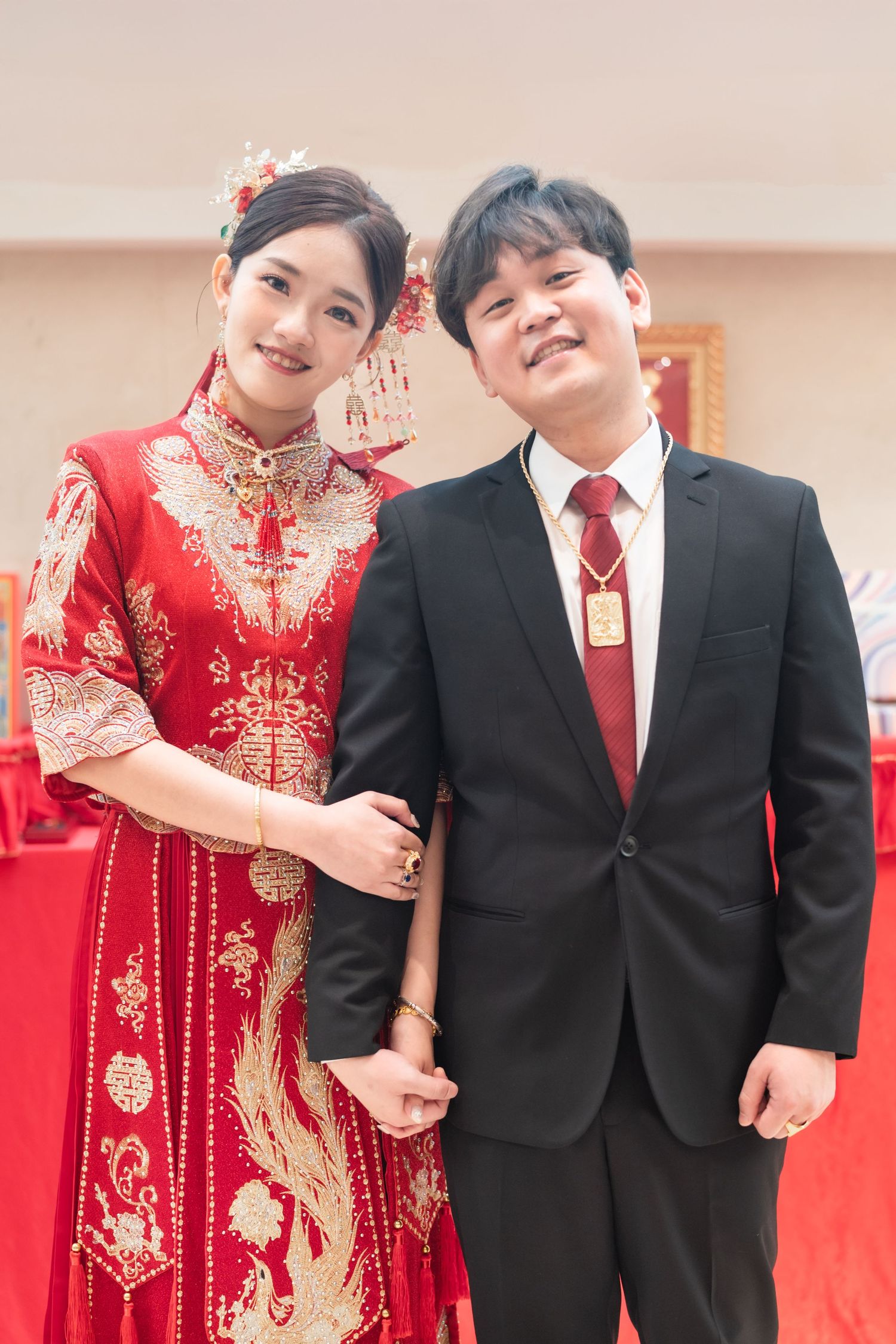 A couple in traditional wedding attire with the bride wearing a red qipao dress and groom in black suit with red tie.