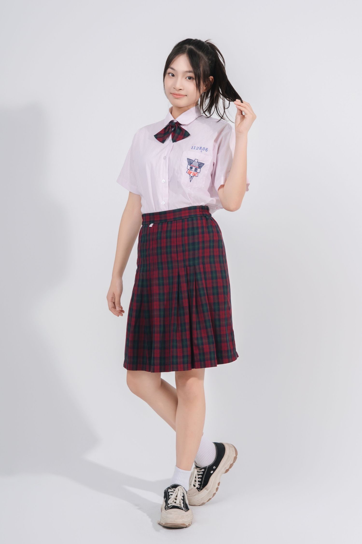A model showcases a white polo shirt paired with a red plaid pleated skirt and casual sneakers against a white background.