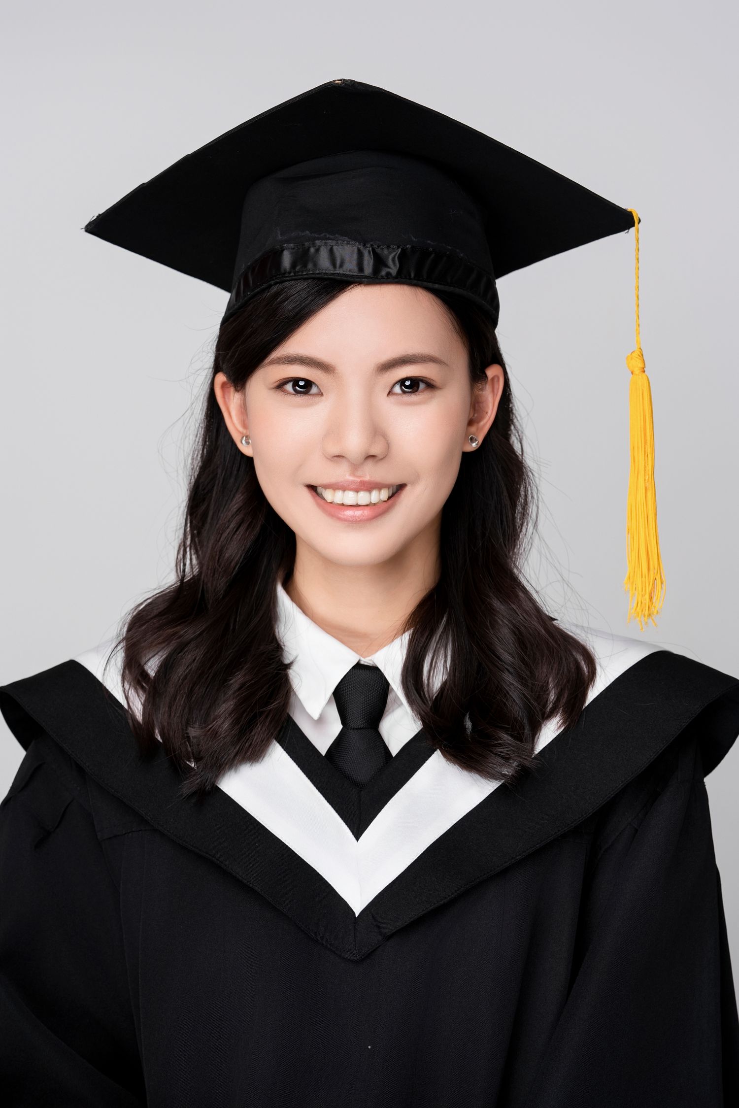 Graduate wearing traditional black cap and gown with white collar and black tie smiles brightly in graduation photos.