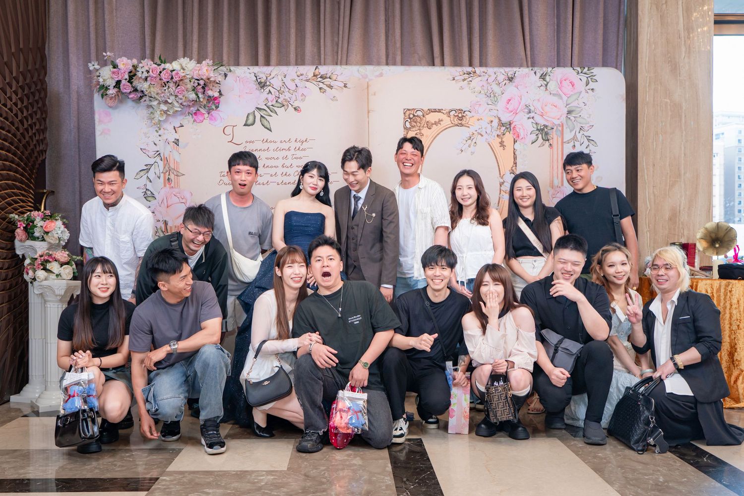 Group of people posing together at a wedding reception with floral backdrop decorations.