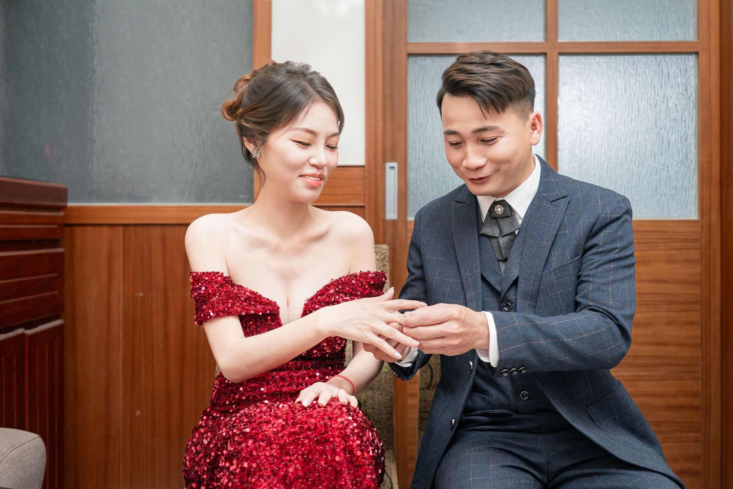 A couple in formal attire shares a tender moment during their wedding photoshoot in a wood-paneled room.