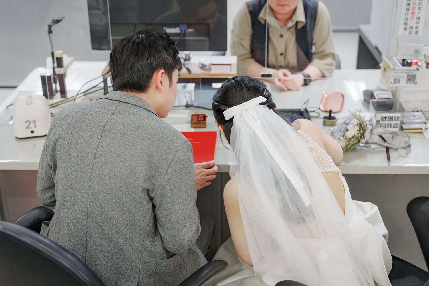 A series of people working at desks in an office environment with papers and documents spread across their workspaces.
