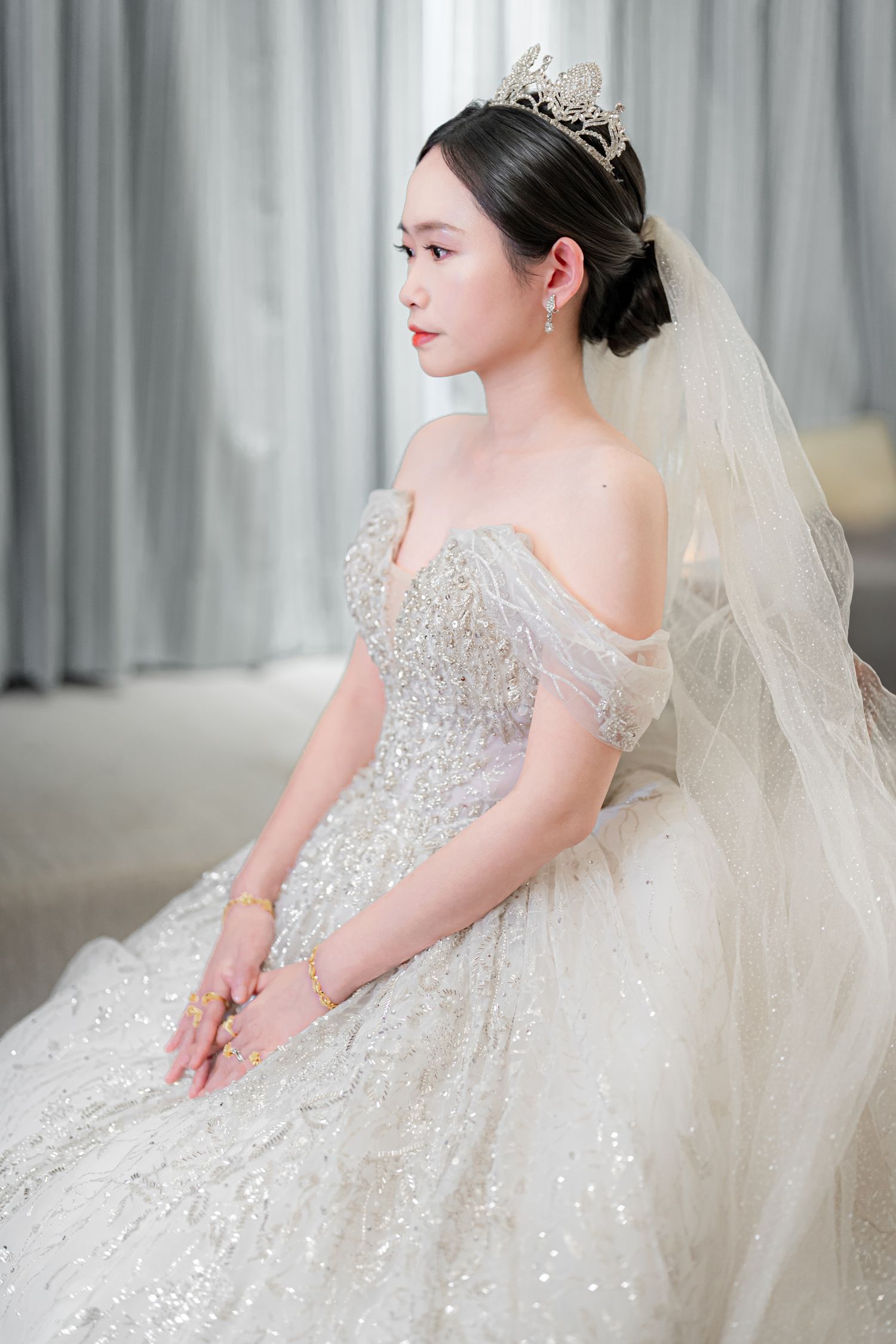 A bride in a sparkling white ball gown with crystal embellishments poses elegantly against a light gray backdrop.