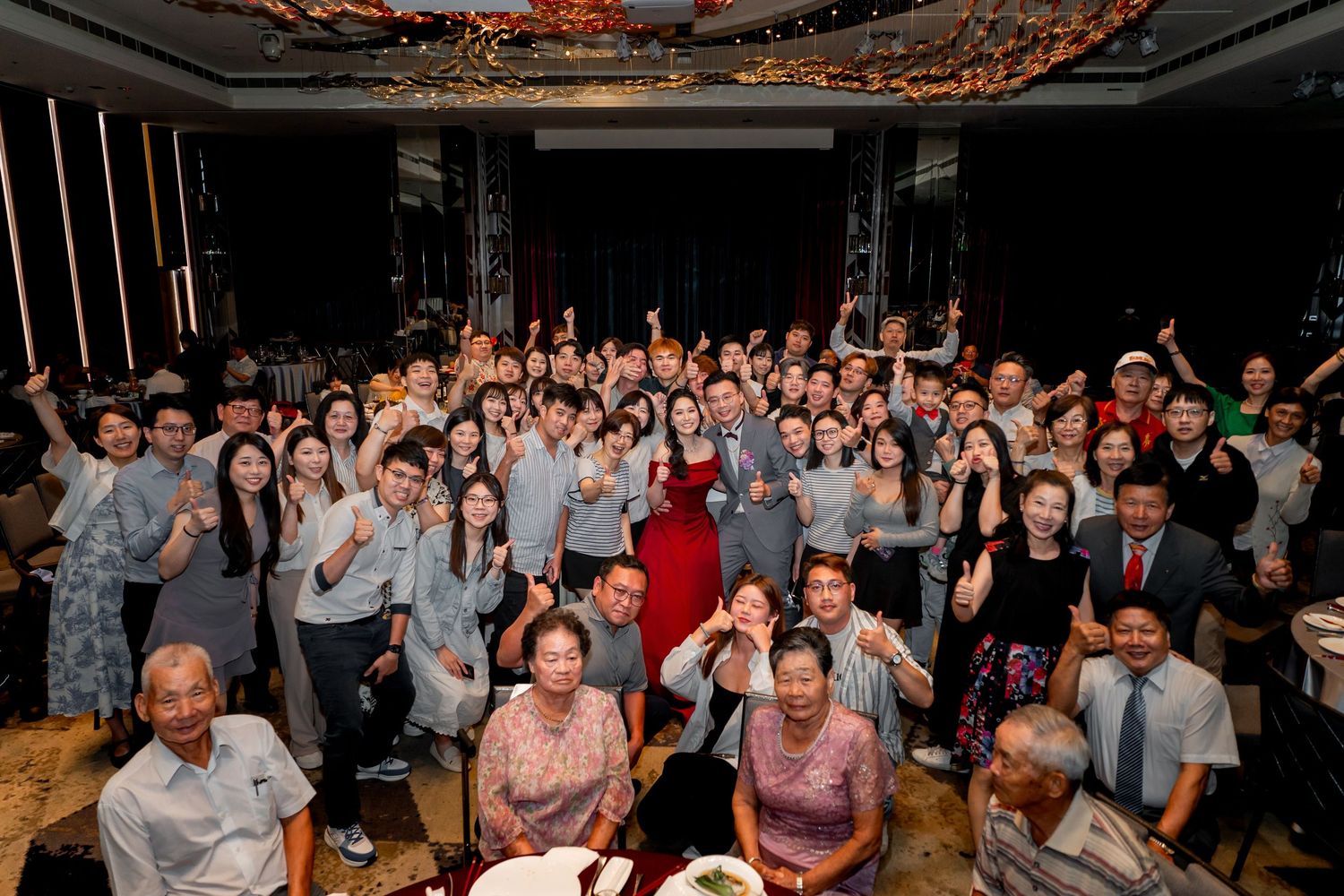 Large group of wedding guests posing together at a celebratory reception in a formal indoor venue.