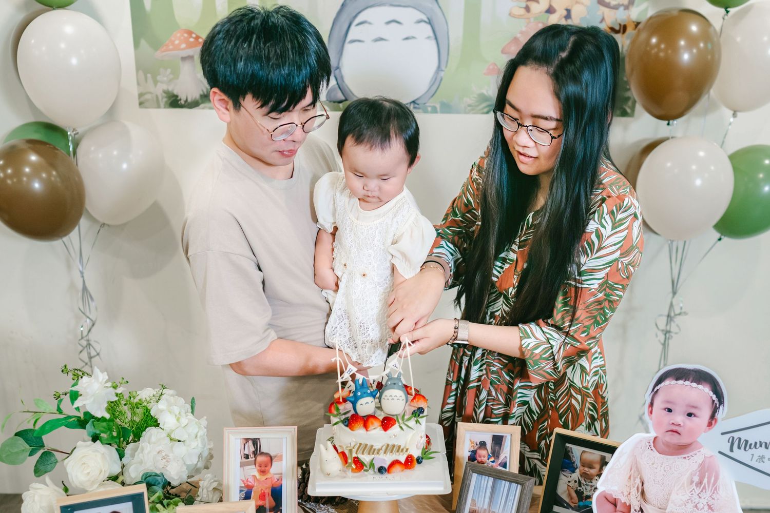 A festive first birthday party scene with white and brown balloons, party decorations, and a cake cutting moment.