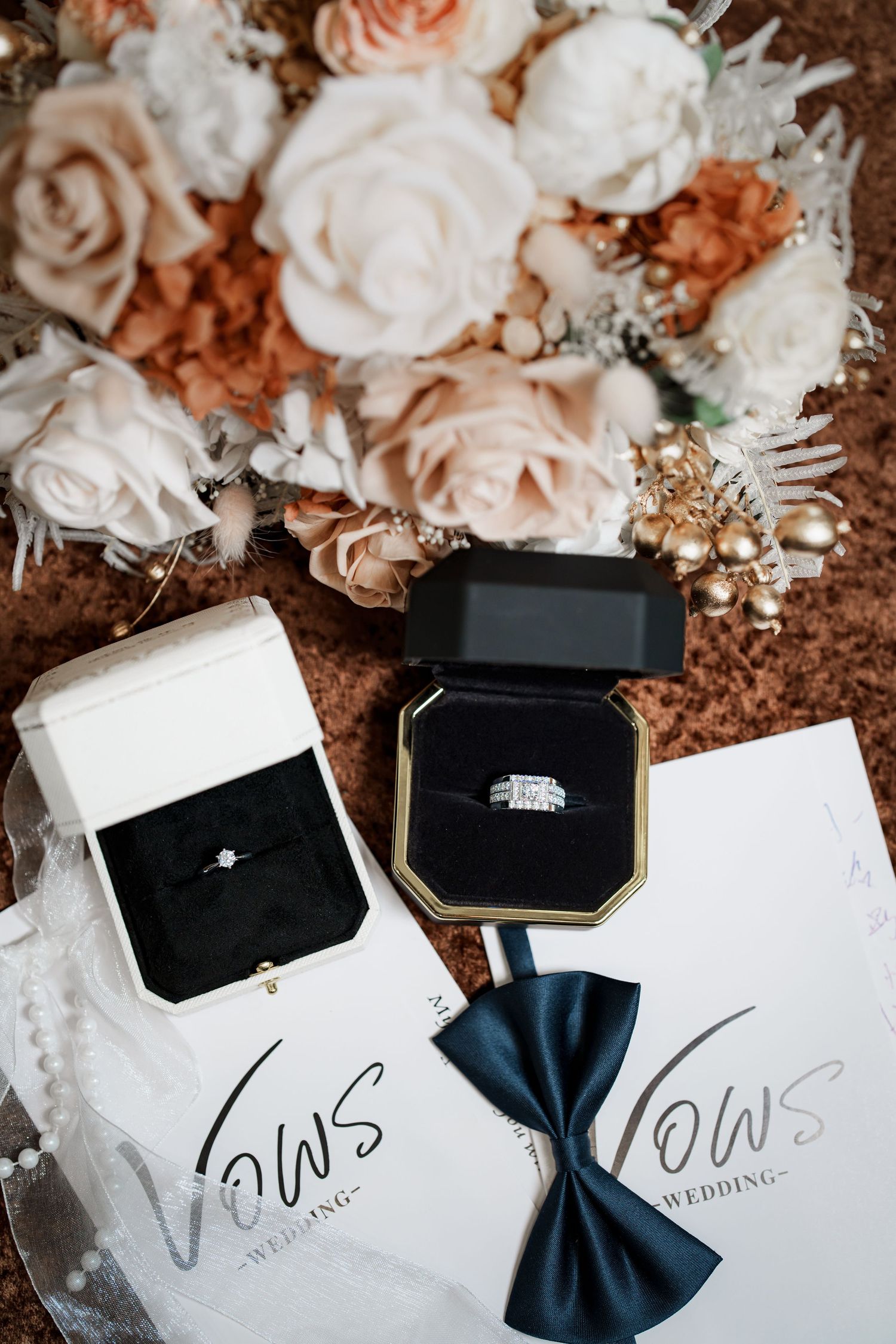 Wedding rings and vows displayed with soft pink and white roses against a rustic brown background.