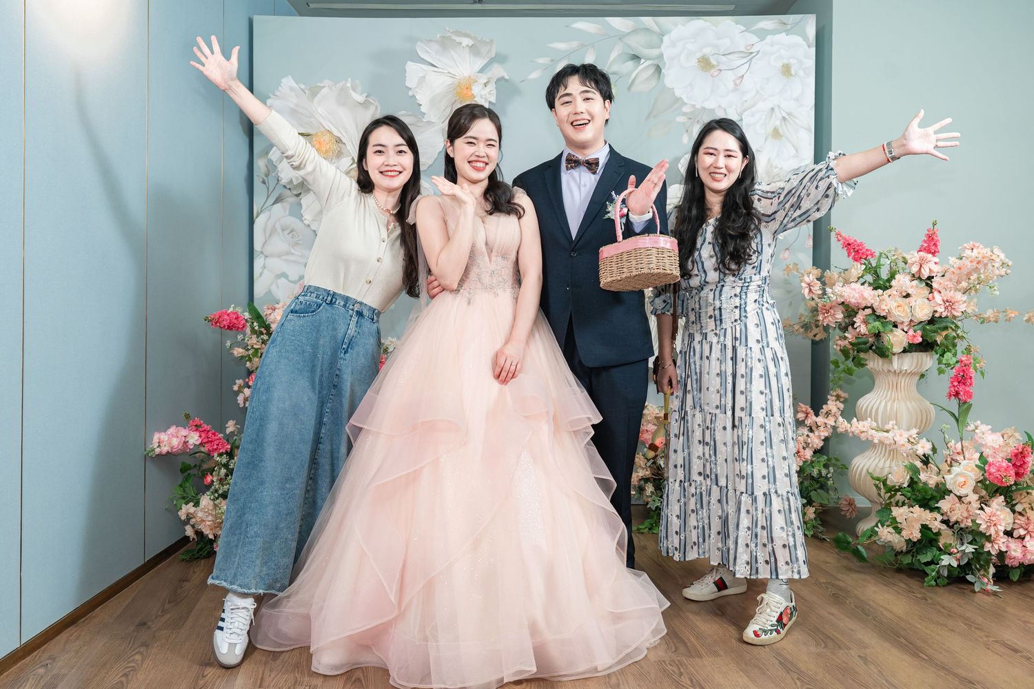 Group poses together against light blue wall with pink floral arrangements at a formal event.