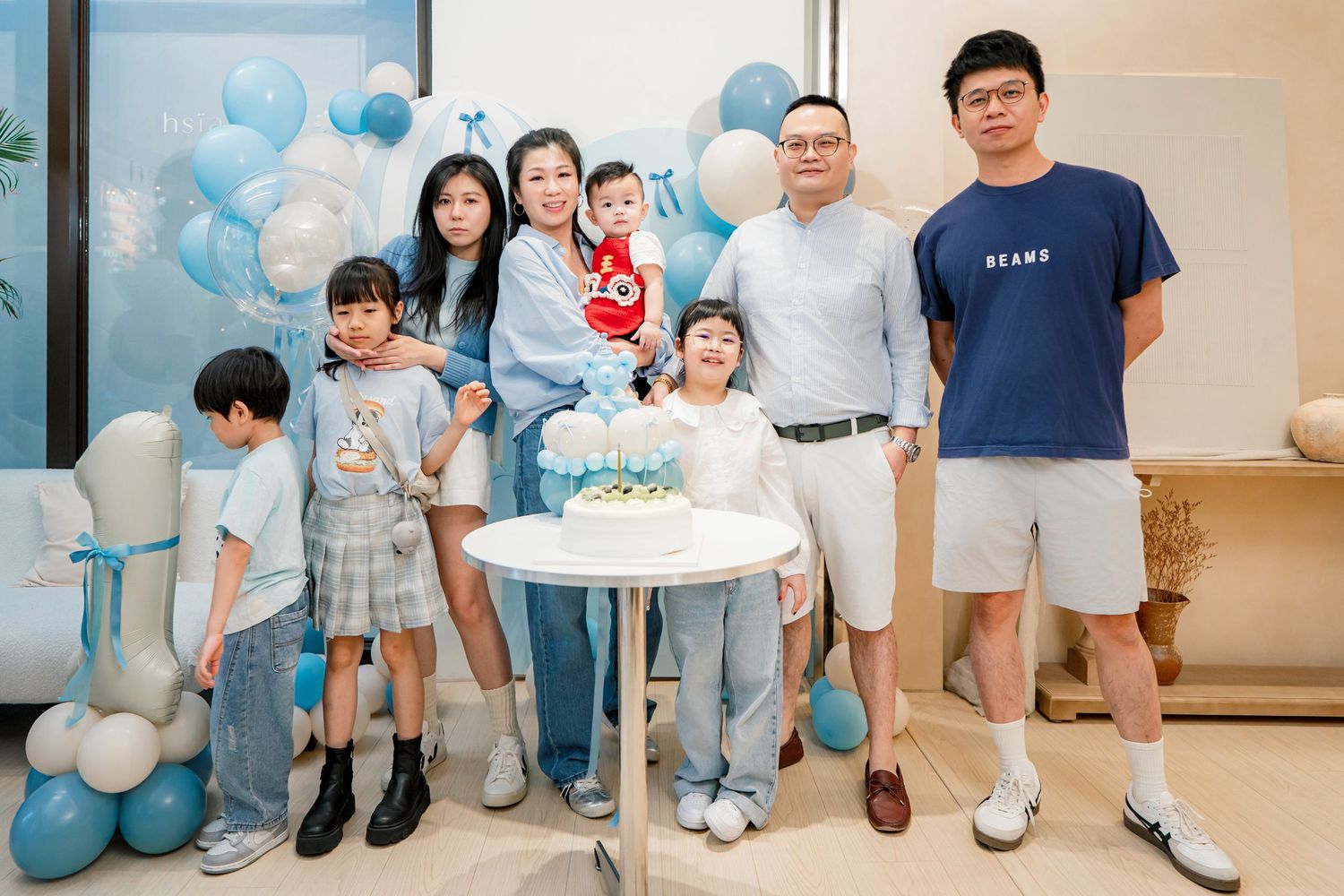 A group of people pose together at a baby shower celebration with blue and white balloon decorations.