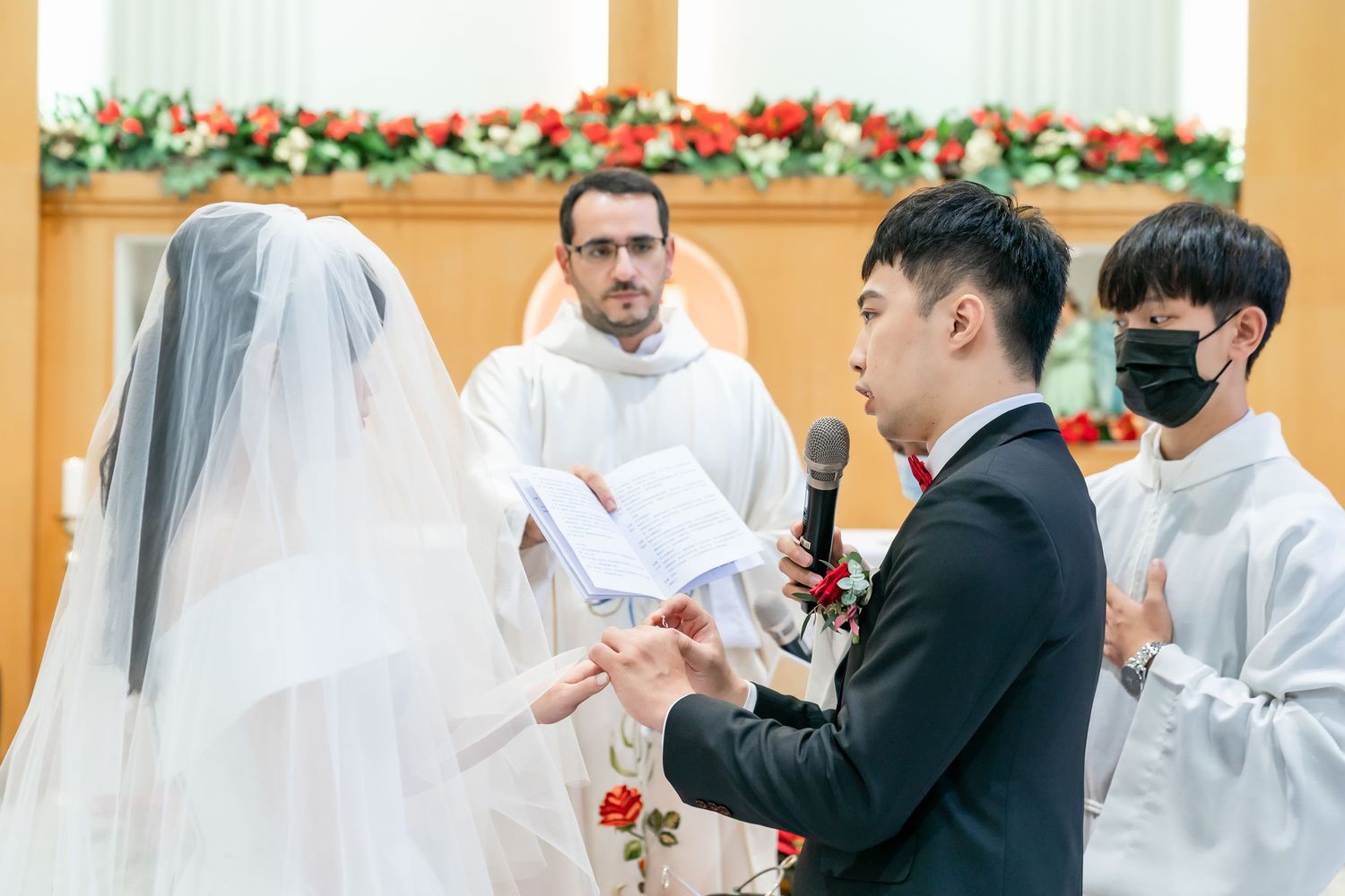 Wedding ceremony in progress with clergy and attendants at a decorated church altar.