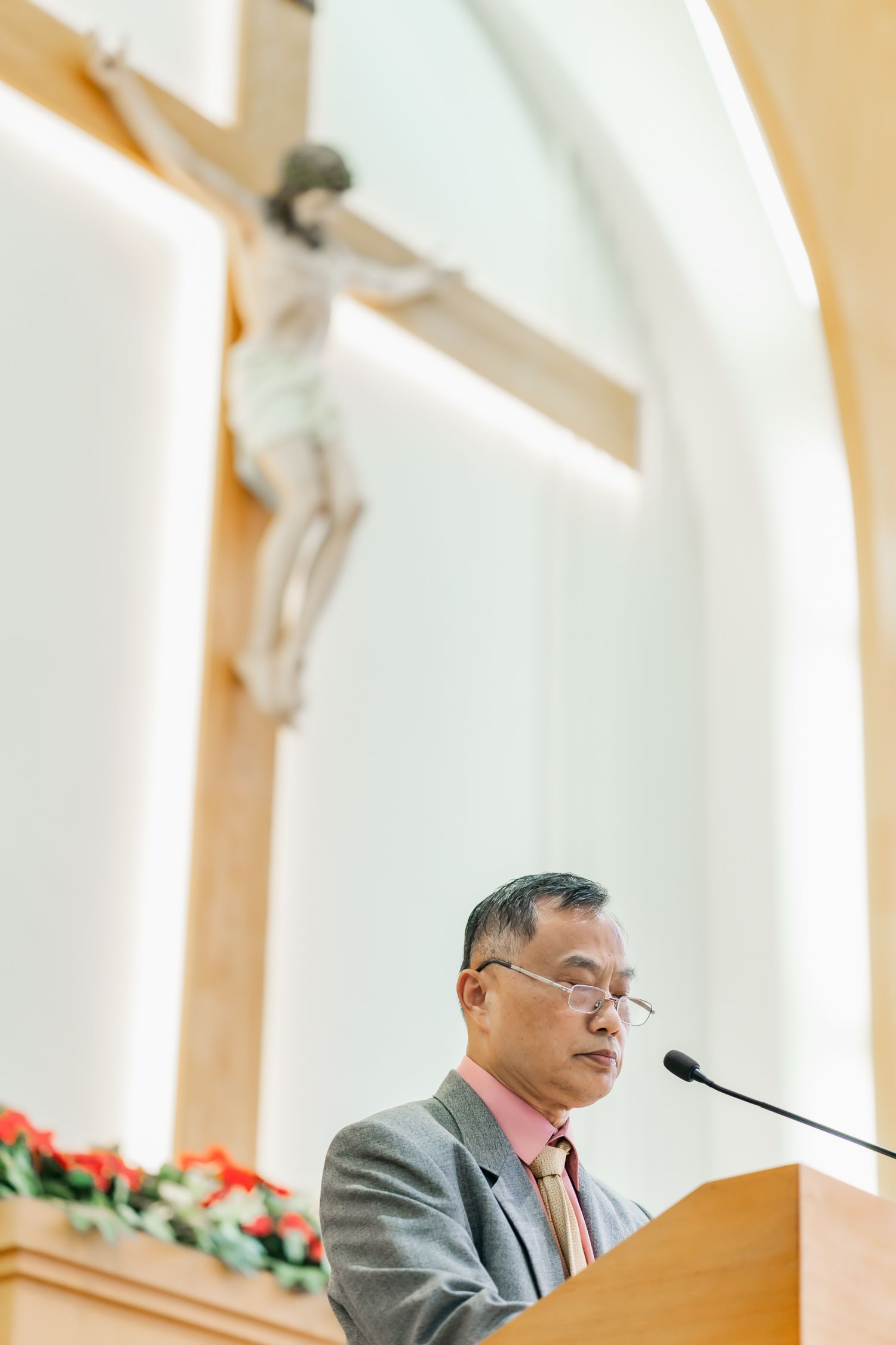 A speaker delivers remarks at a church podium with a crucifix mounted on the wall behind.