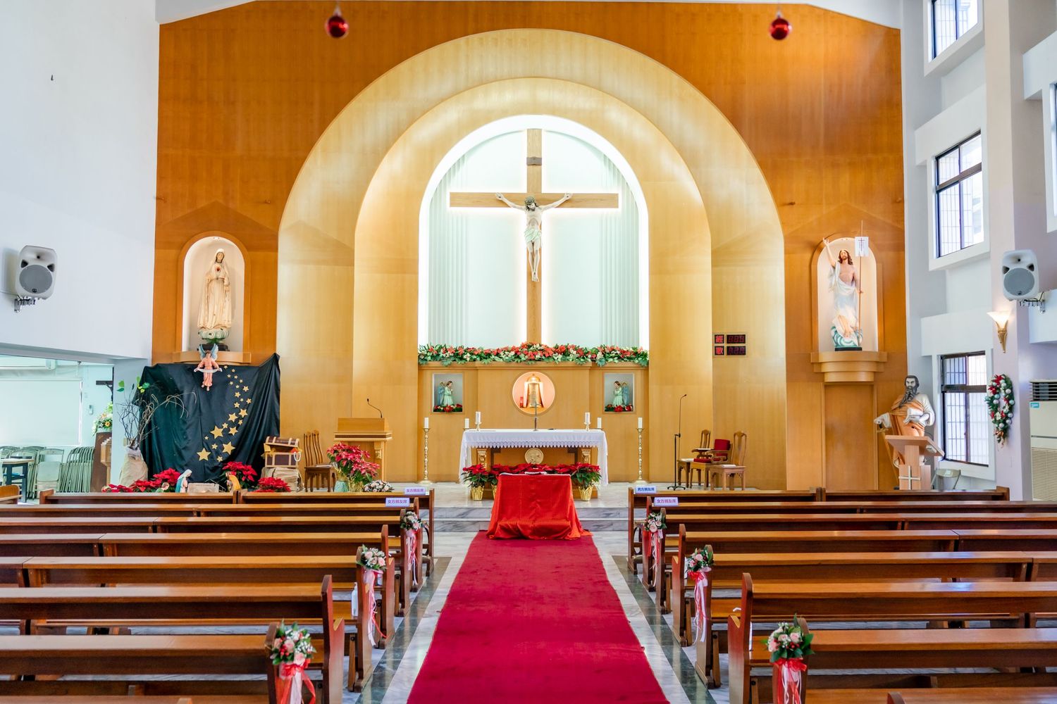 Interior of a church sanctuary with wooden pews and red carpet leading to a cross-adorned altar.