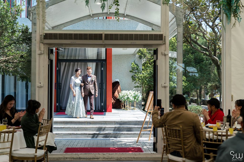 Wide view of wedding ceremony space with guests seated at gold chairs.