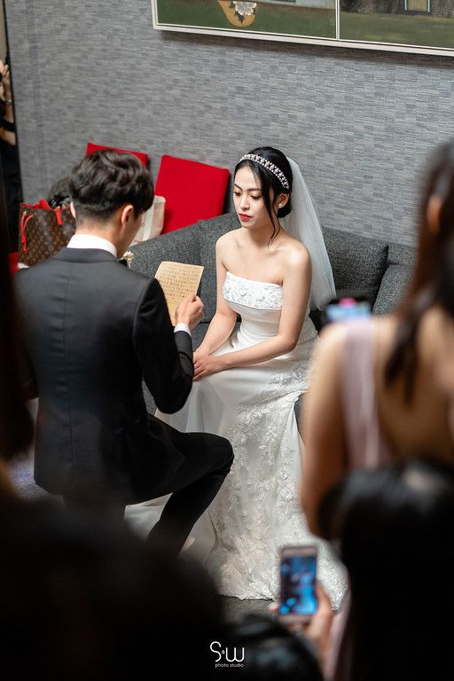 Intimate wedding moment as groom reads vows from card while seated bride listens.