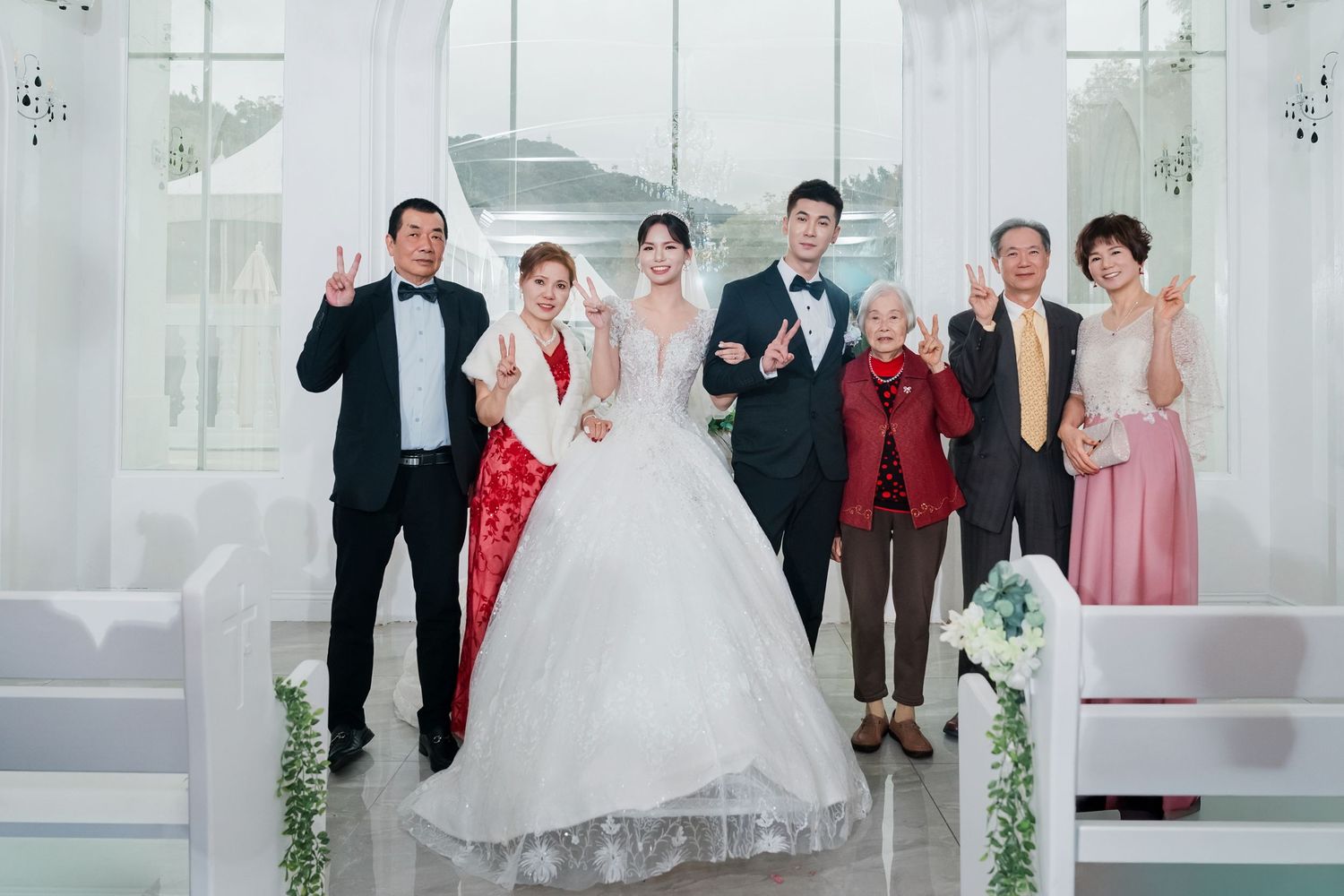 Wedding party poses together in a bright white venue wearing formal attire with bridesmaids in pink dresses.