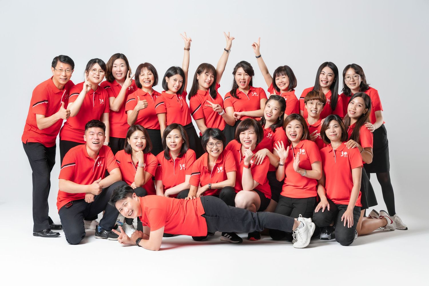 A group in matching red polo shirts poses together against a white backdrop for a team photo.