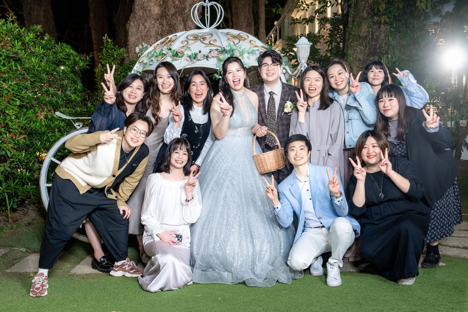 A wedding celebration group poses together under a decorative garden arch during an outdoor evening event.